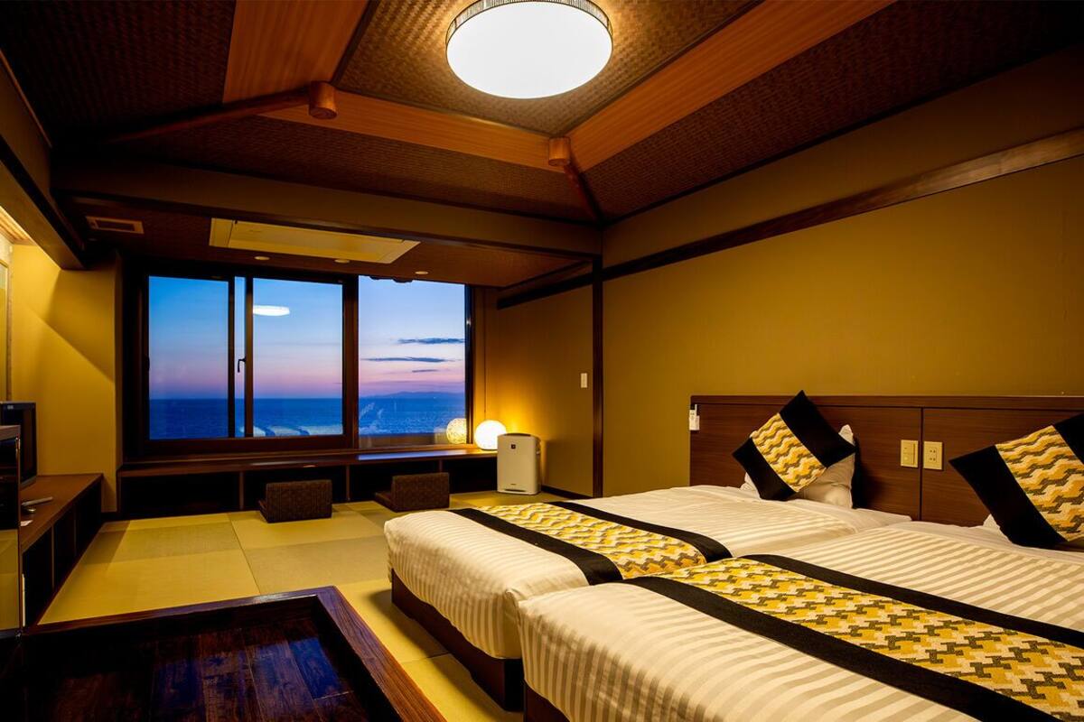 Ein Hotelzimmer mit zwei Betten, einem Fernseher, einem Schreibtisch und Meerblick.