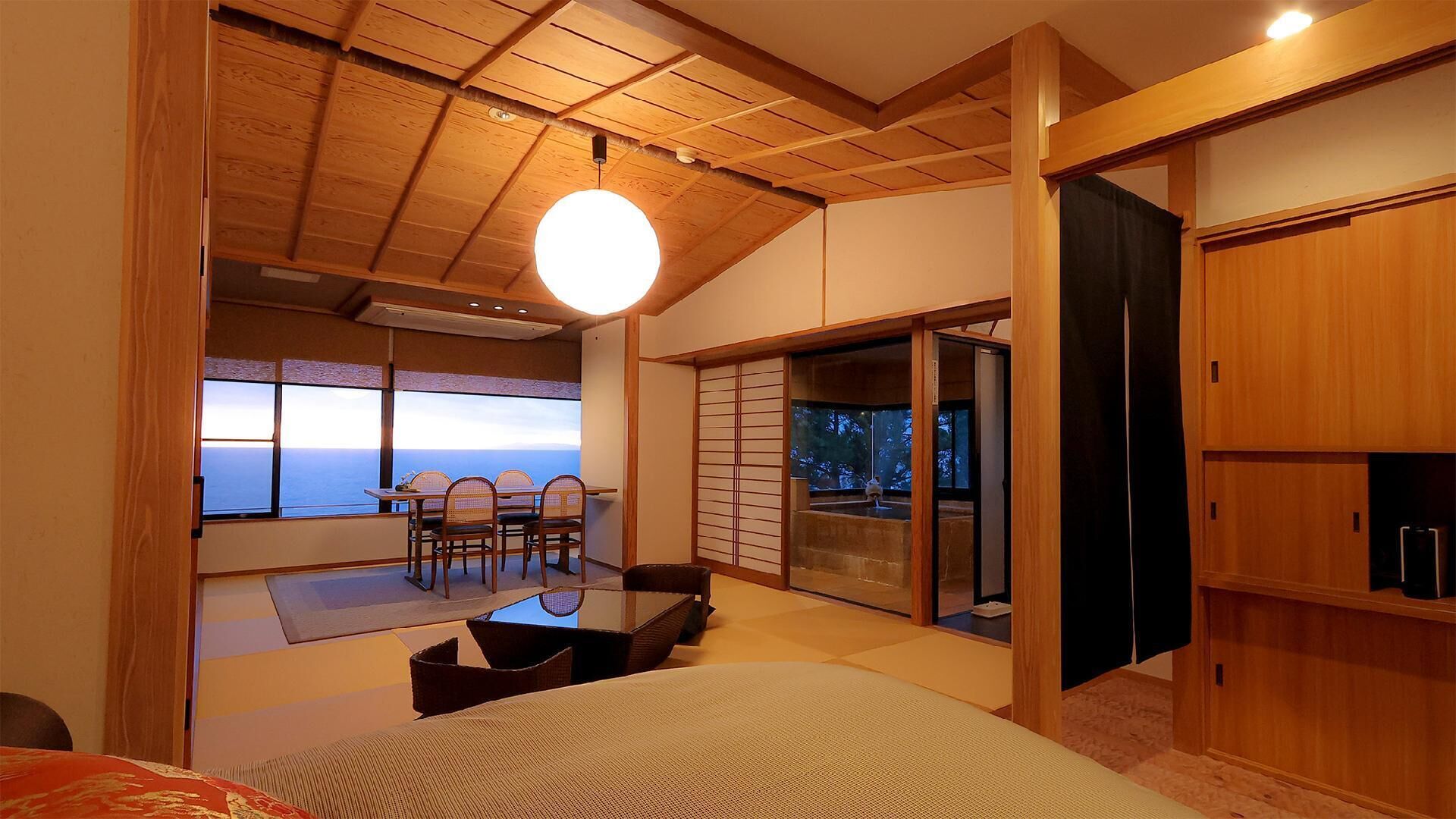 A room with a view of the ocean, a dining area with chairs, and a sliding door leading to a balcony.