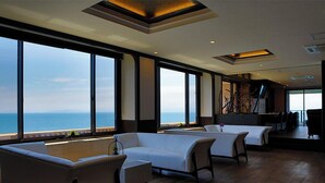 A spacious room with large windows offering a view of the sea, a dining area with chairs, and a modern ceiling design.