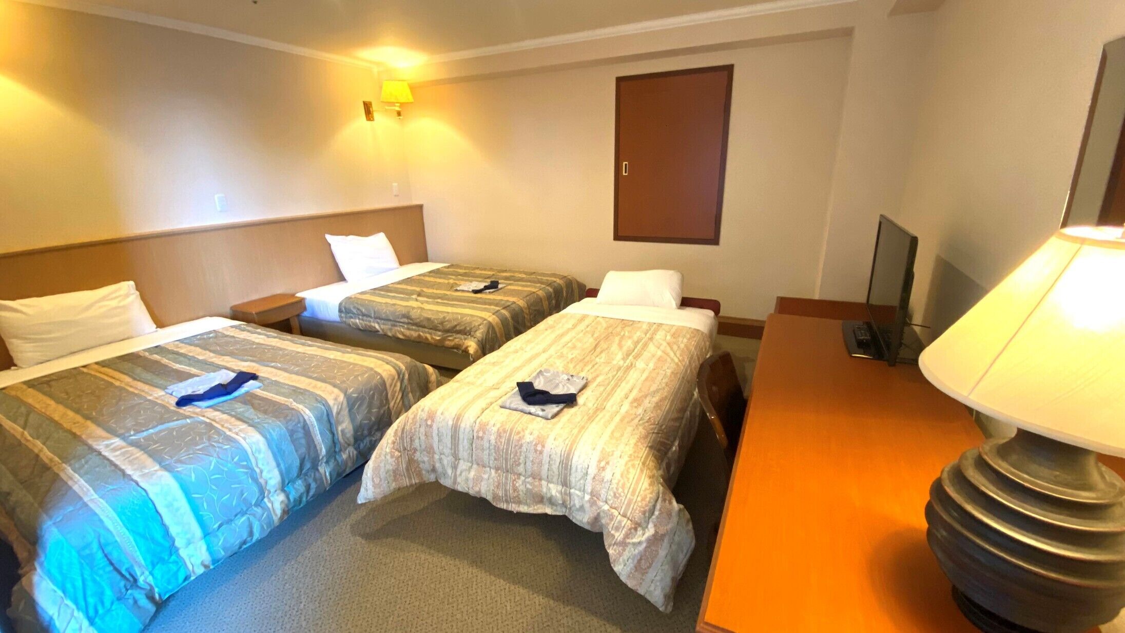 Habitació d'hotel amb dos llits, un escriptori, una làmpada i una televisió.