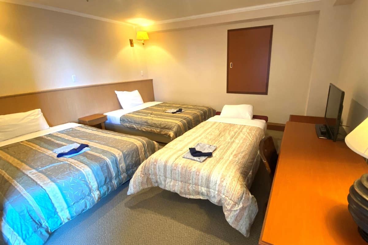 A hotel room with two beds, a desk, a lamp, and a TV.