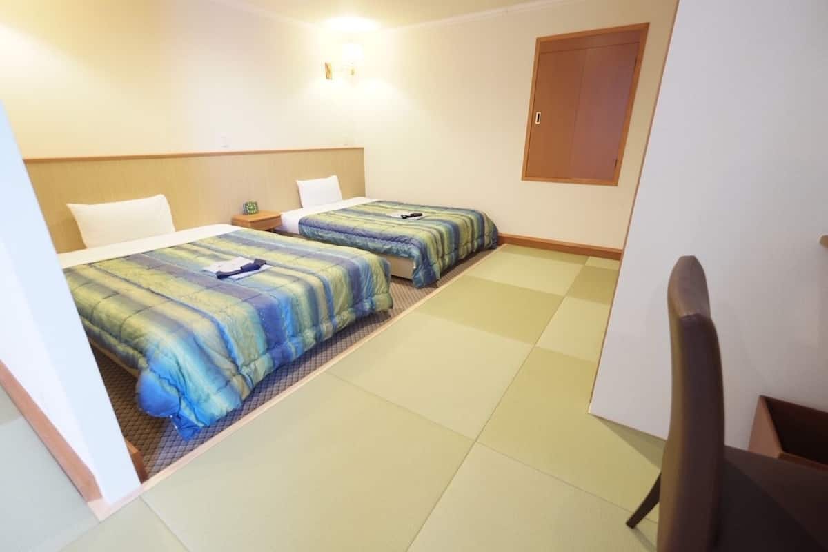 A hotel room with two beds, a wooden headboard, a small bedside table, and a wardrobe.