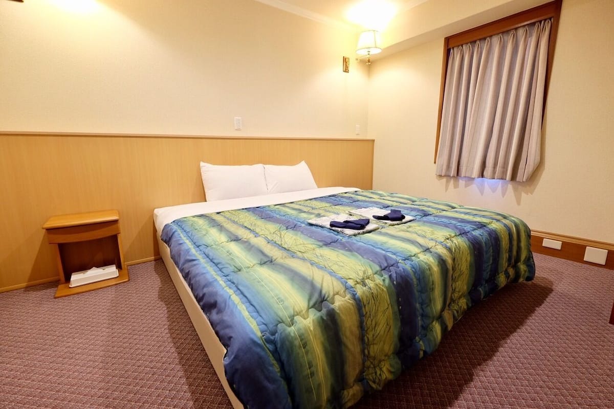 A hotel room with a bed, a nightstand, a lamp, and a window with curtains.