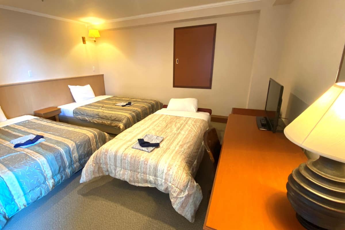 A hotel room with two beds, a desk, a lamp, and a door.