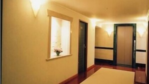 A hallway with a light-colored carpet, a small window with a flower vase, and a door with a dark frame. - Station Hotel Au (Tsu)