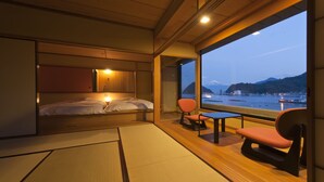 A room with a bed, a table, and chairs, a view of a body of water and mountains, and tatami mats on the floor. - Izu Mitsuhama Syoutoukan (Numazu)
