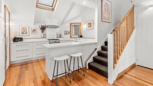 A modern kitchen with white cabinetry, a wooden staircase, and a lofted ceiling with a skylight. - Seahaven Village (Barwon Heads)