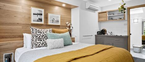 Quarto moderno com cabeceira de madeira, cama com manta cor mostarda e mesa de cabeceira com cafeteira.