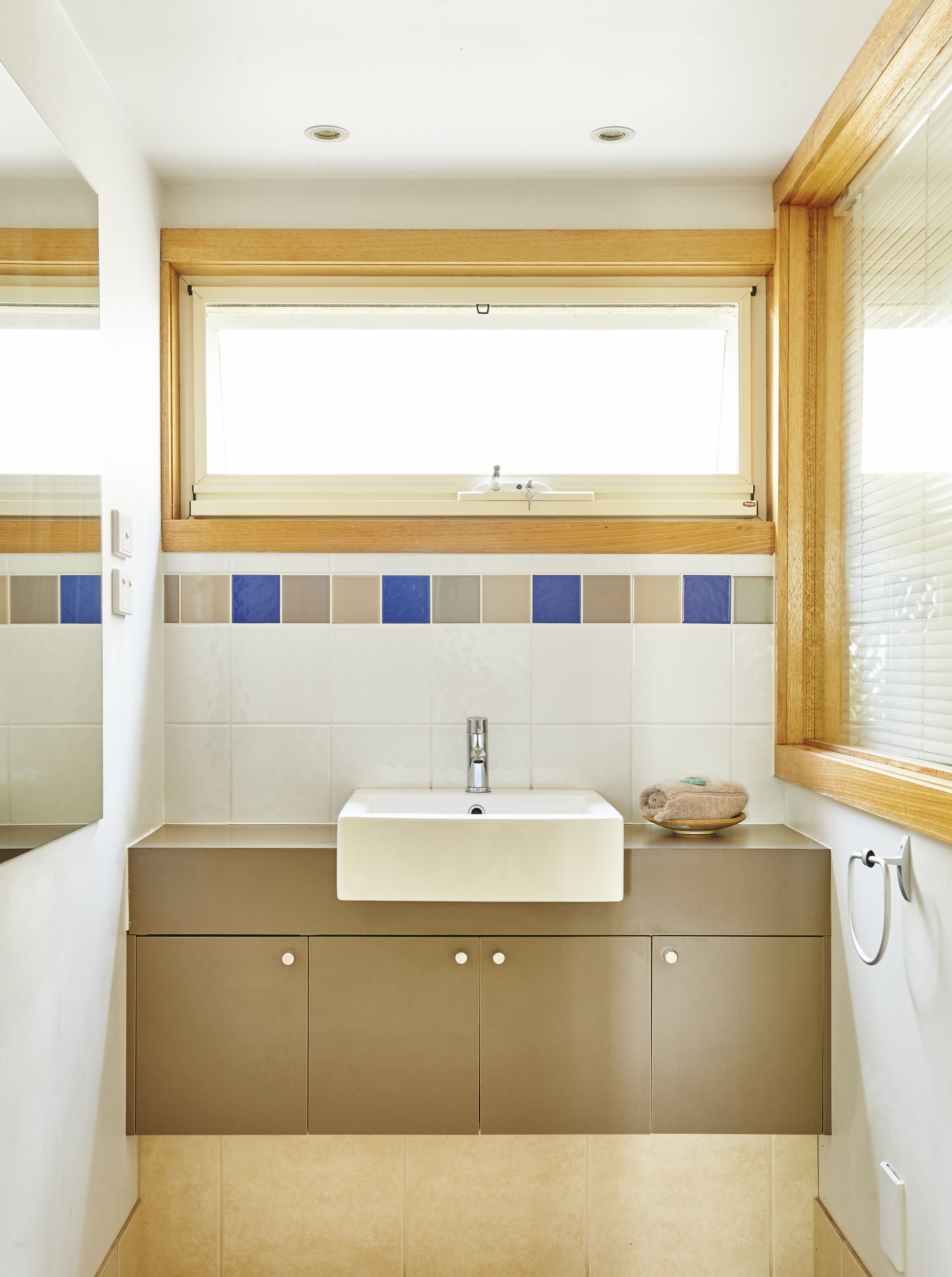 A bathroom with a rectangular sink, wooden window frame, and tiled backsplash.