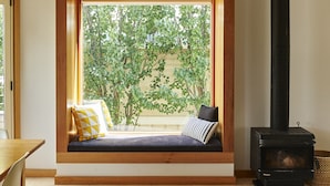 A cozy room with a built-in bench under a large window, a black wood-burning stove, and a wooden ceiling. - Seahaven Village (Barwon Heads)