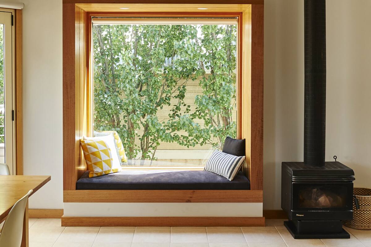 A cozy room with a built-in bench under a large window, a black wood-burning stove, and a wooden ceiling.