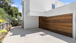 A modern house with a white exterior, a wooden garage door, and a small window. - Seahaven Village (Barwon Heads)