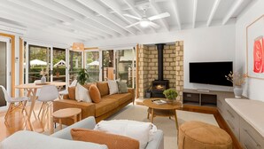 A modern living room with a sofa, coffee table, and TV. There's a fireplace, a ceiling fan, and a stone wall. - Seahaven Village (Barwon Heads)