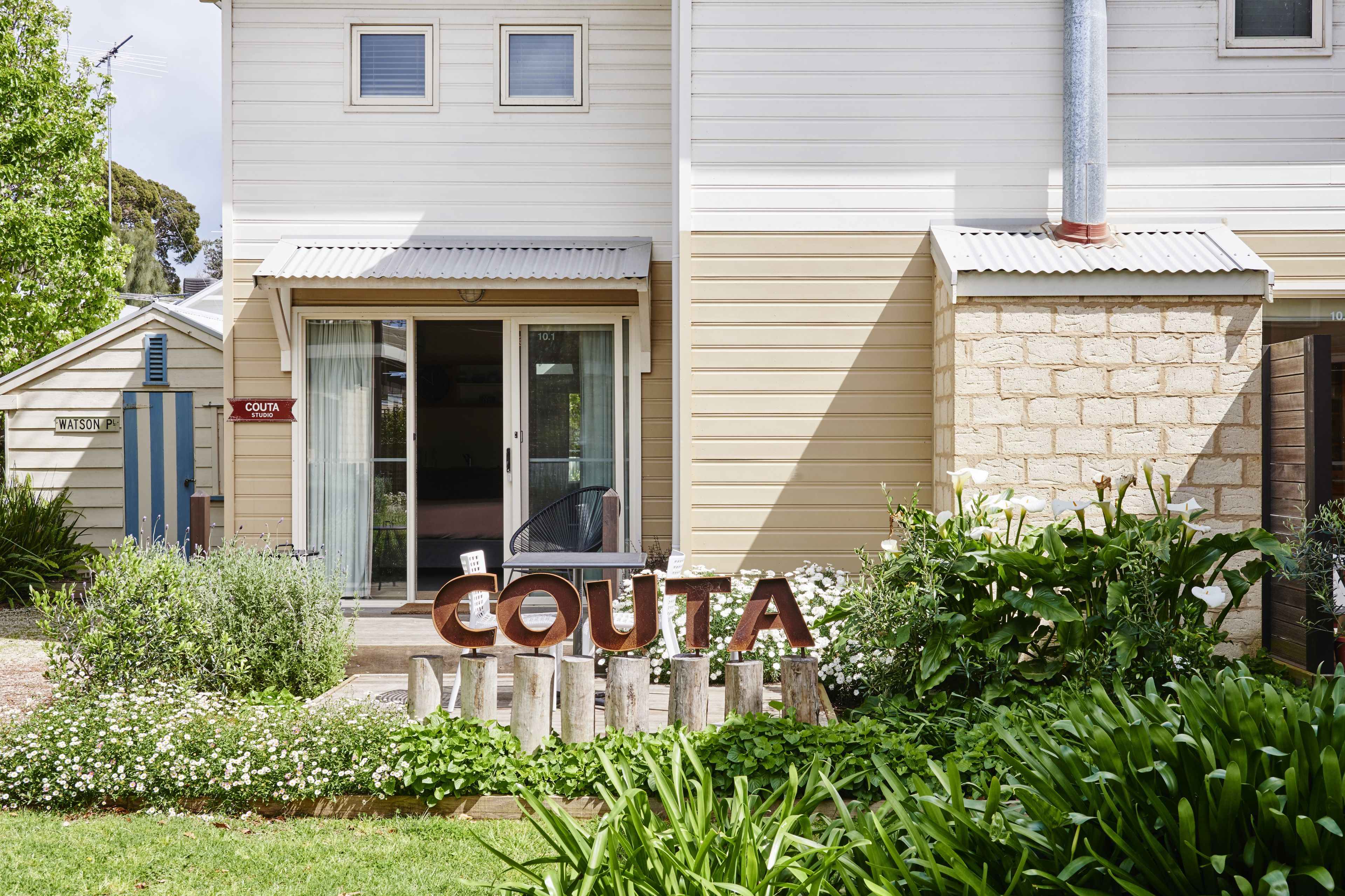 A building with a sign reading "COUTA" in front, a covered entrance, and a brick wall on the right.