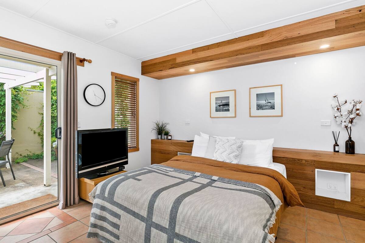 A modern bedroom with a wooden headboard, a flat-screen TV, a bed with a patterned blanket, and two framed pictures on the wall.
