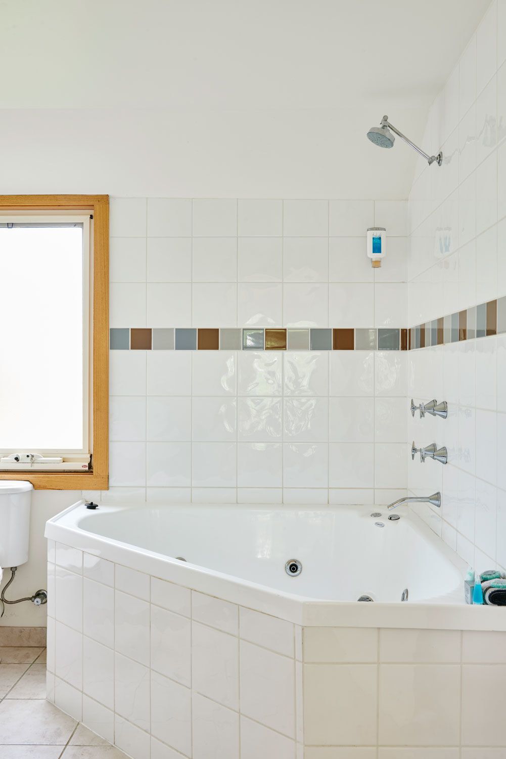 A modern bathroom with a freestanding bathtub, a window with a wooden frame, and a tiled backsplash with a mosaic pattern.