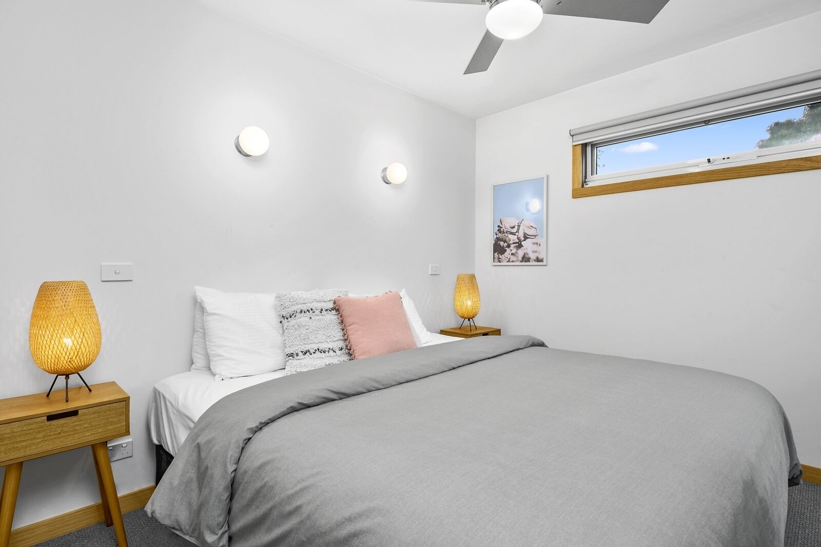 A modern bedroom with a bed, bedside lamps, a ceiling fan, and a window with a view.