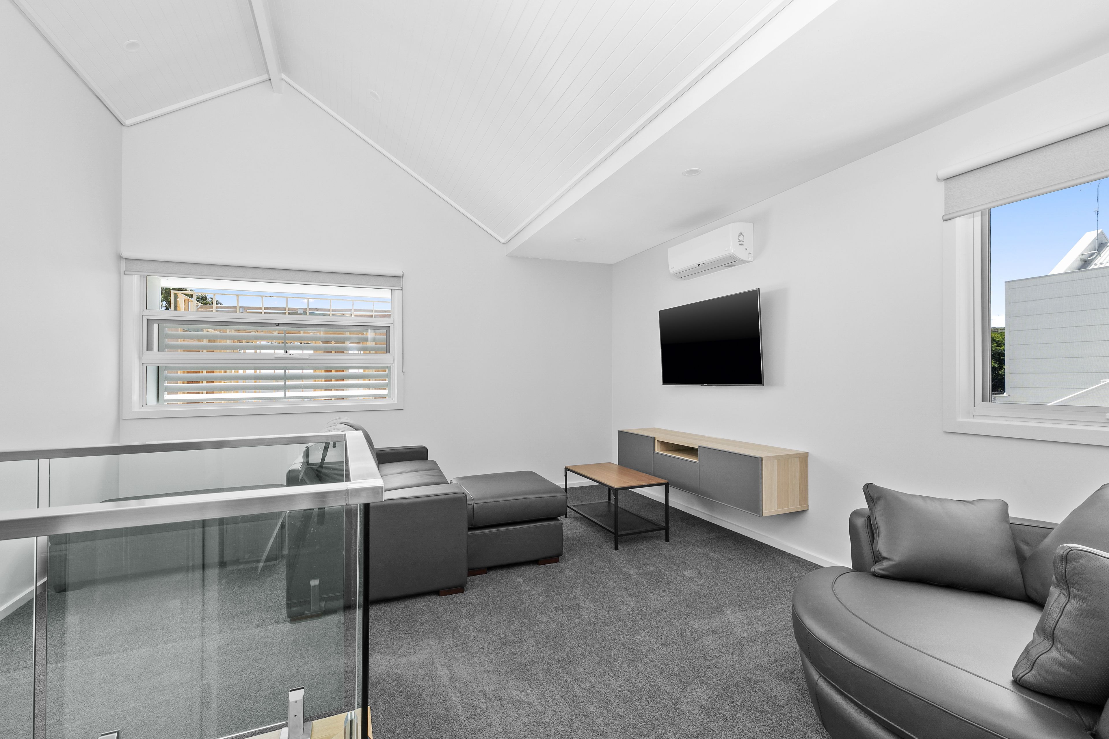 A modern living room with a glass partition, grey sofas, a wooden coffee table, and a mounted TV.