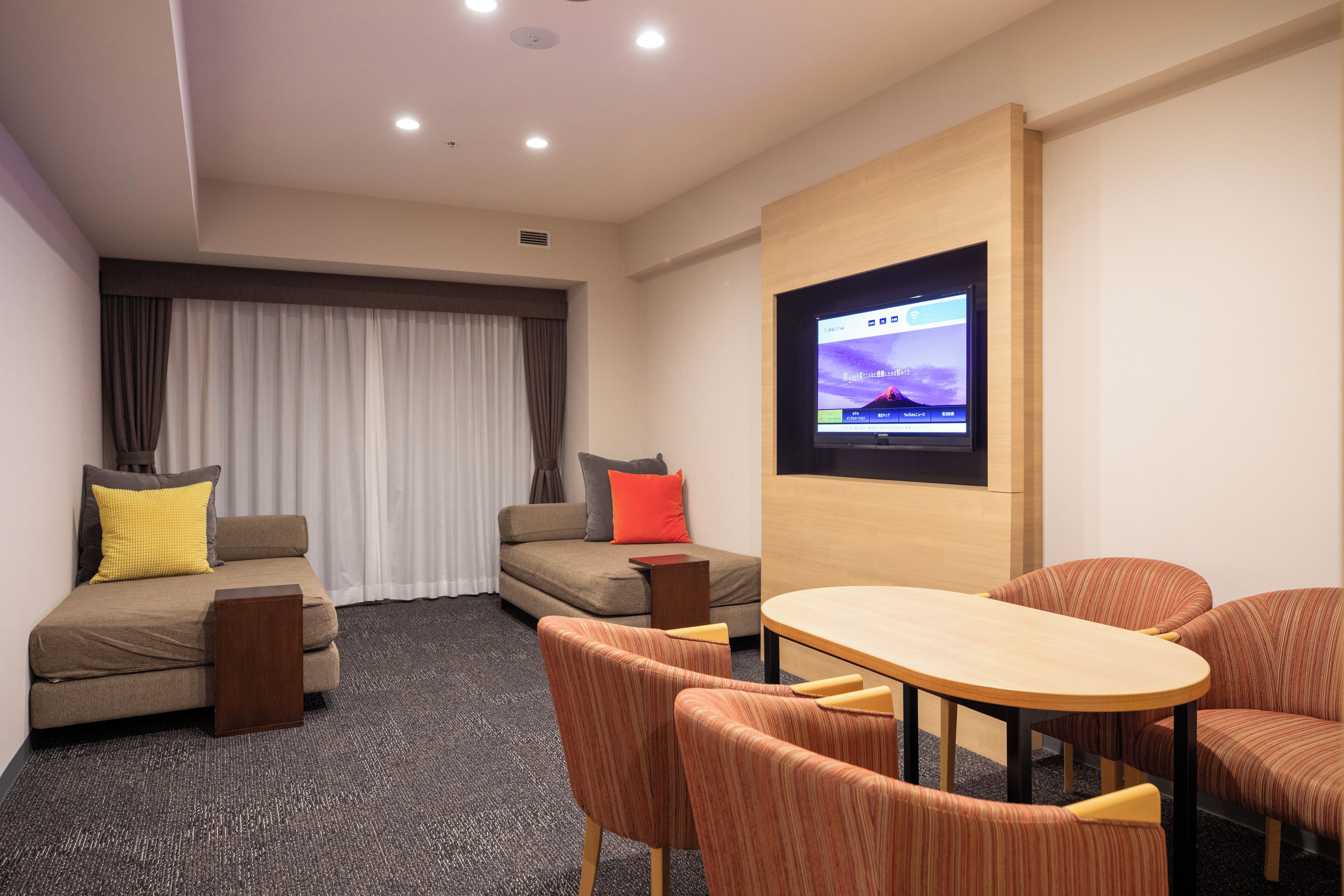 Ein modernes Hotelzimmer mit einer Couch, einem kleinen Tisch und zwei Sesseln. Ein Flachbildfernseher ist an der Wand befestigt.