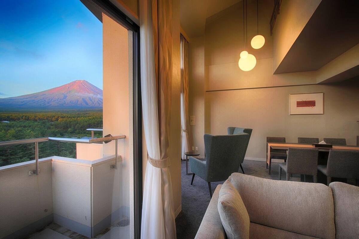 Habitación de hotel con balcón, zona de comedor y vistas a la montaña.