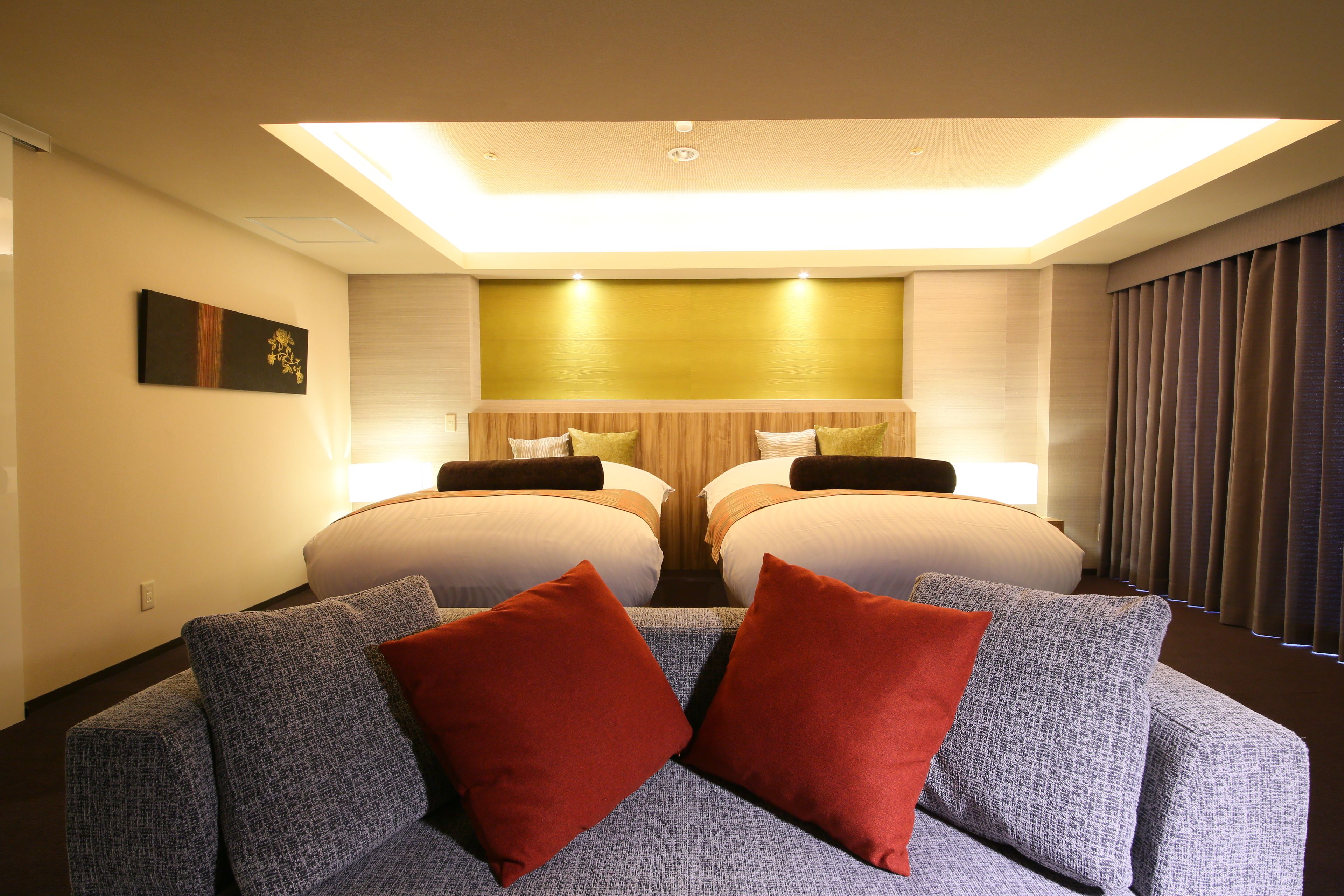 A hotel room with two beds, a sofa, and a ceiling light.