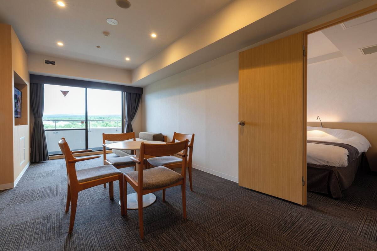 Una habitación de hotel con comedor, cama y vista a través de un ventanal grande.
