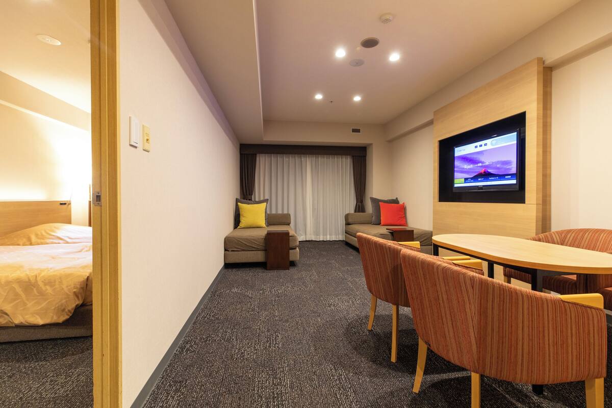 Habitación de hotel con cama, sofá, una mesita, televisor y piso alfombrado.