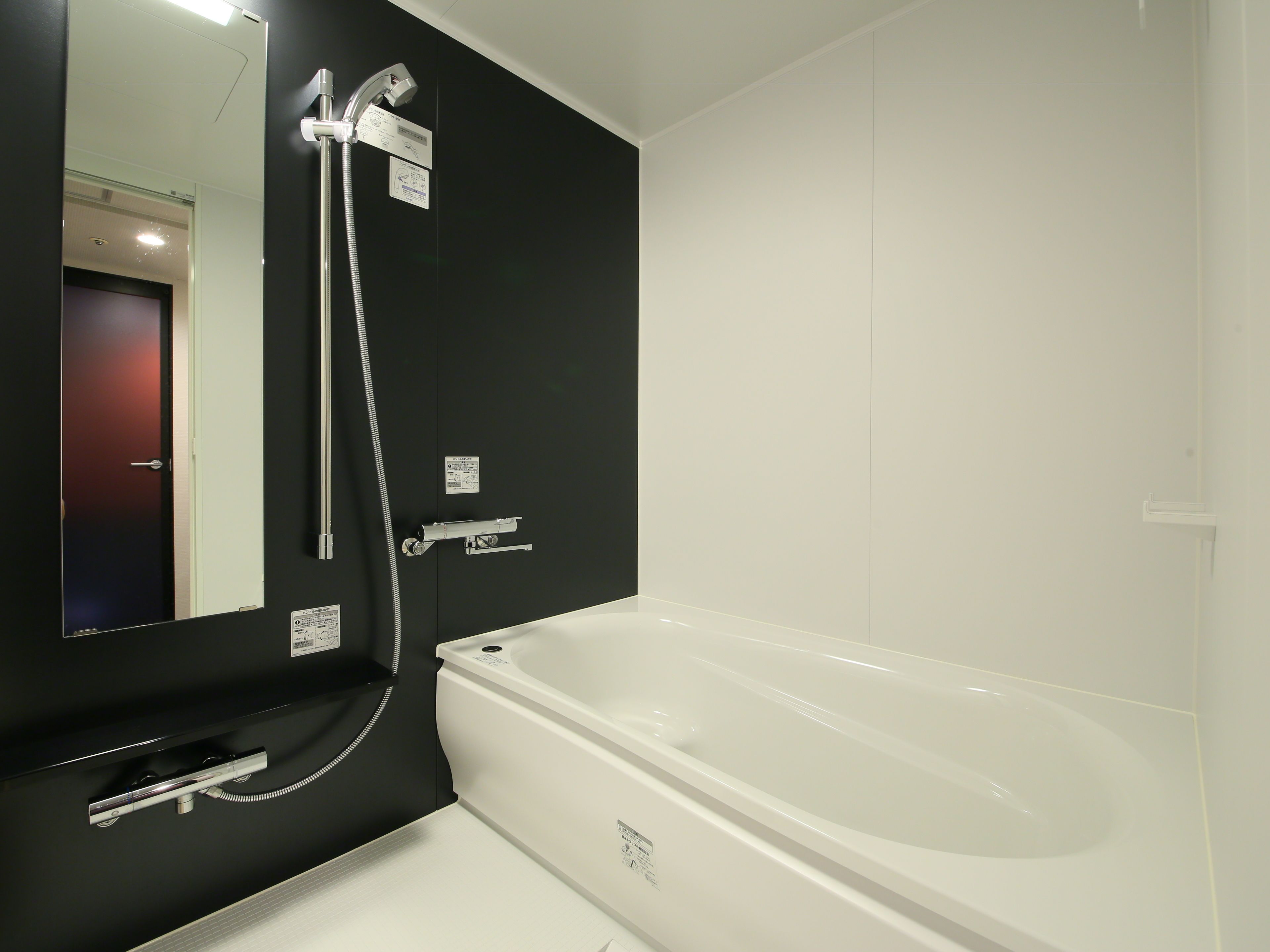 Un baño moderno con una bañera blanca, un espejo grande y una pared negra.