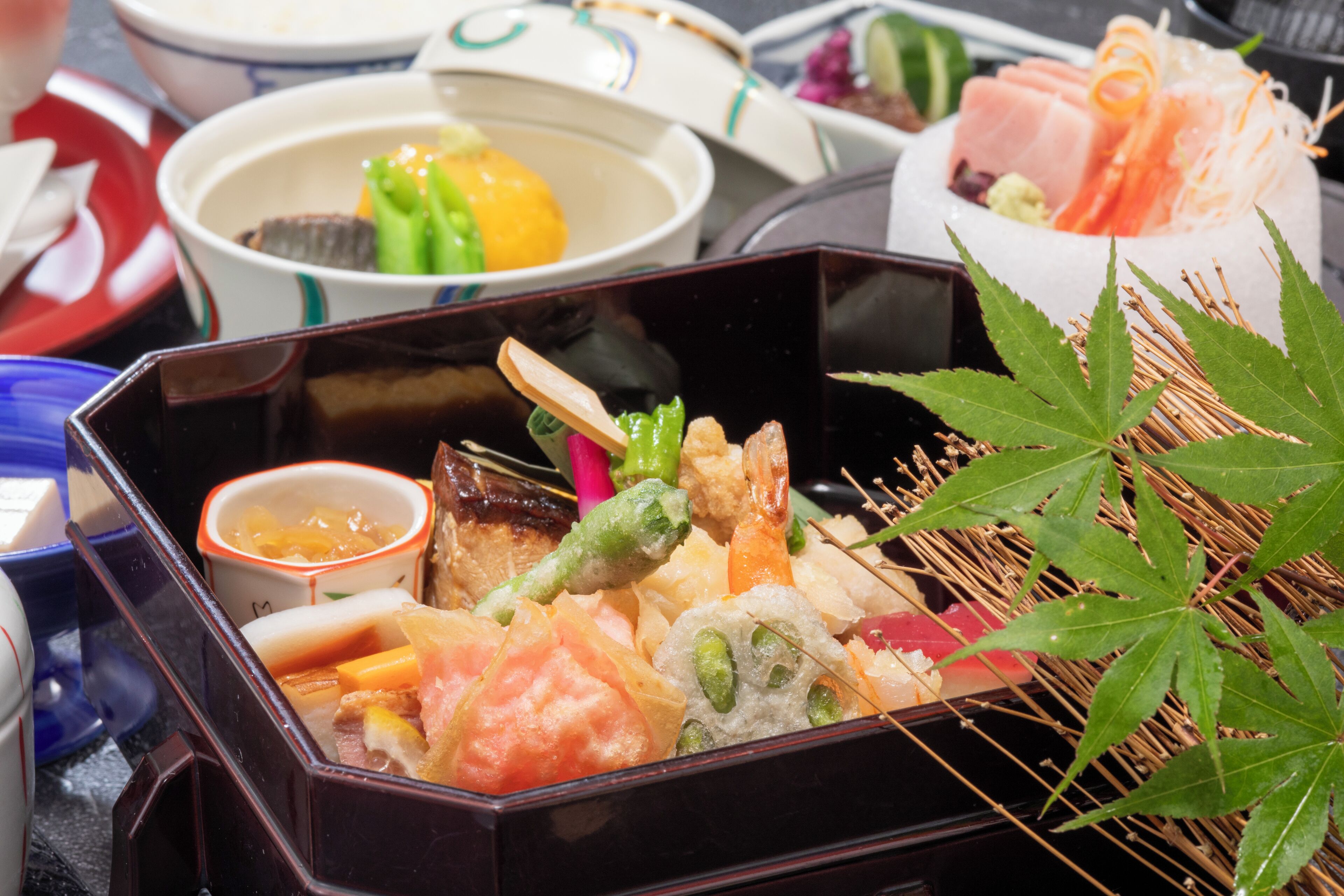 Una caja bento japonesa tradicional con diferentes alimentos y una hoja decorativa.
