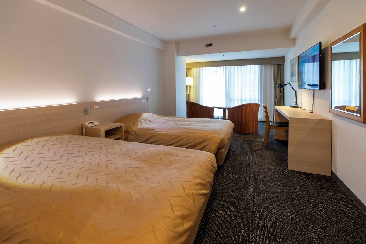 Habitación de hotel con dos camas, un escritorio, una silla, un televisor y una ventana con cortinas.