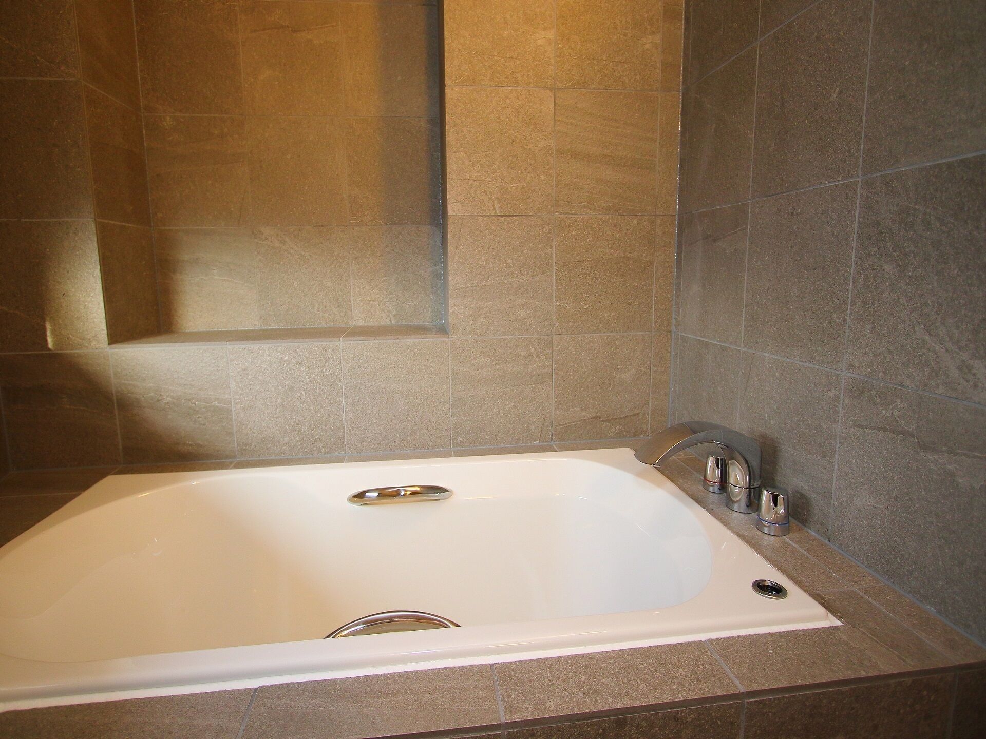 A bathroom with a large bathtub, a modern faucet, and a showerhead.