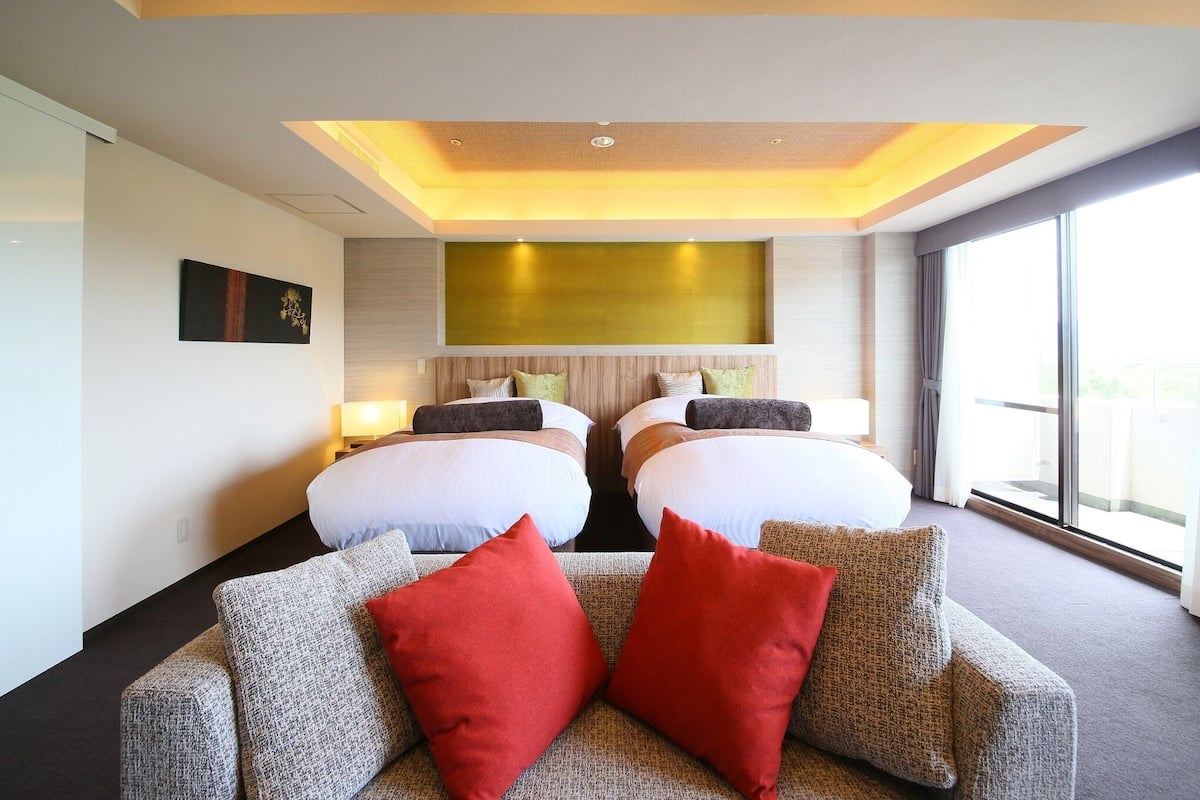 Habitación de hotel con dos camas, un sofá y un ventanal grande.