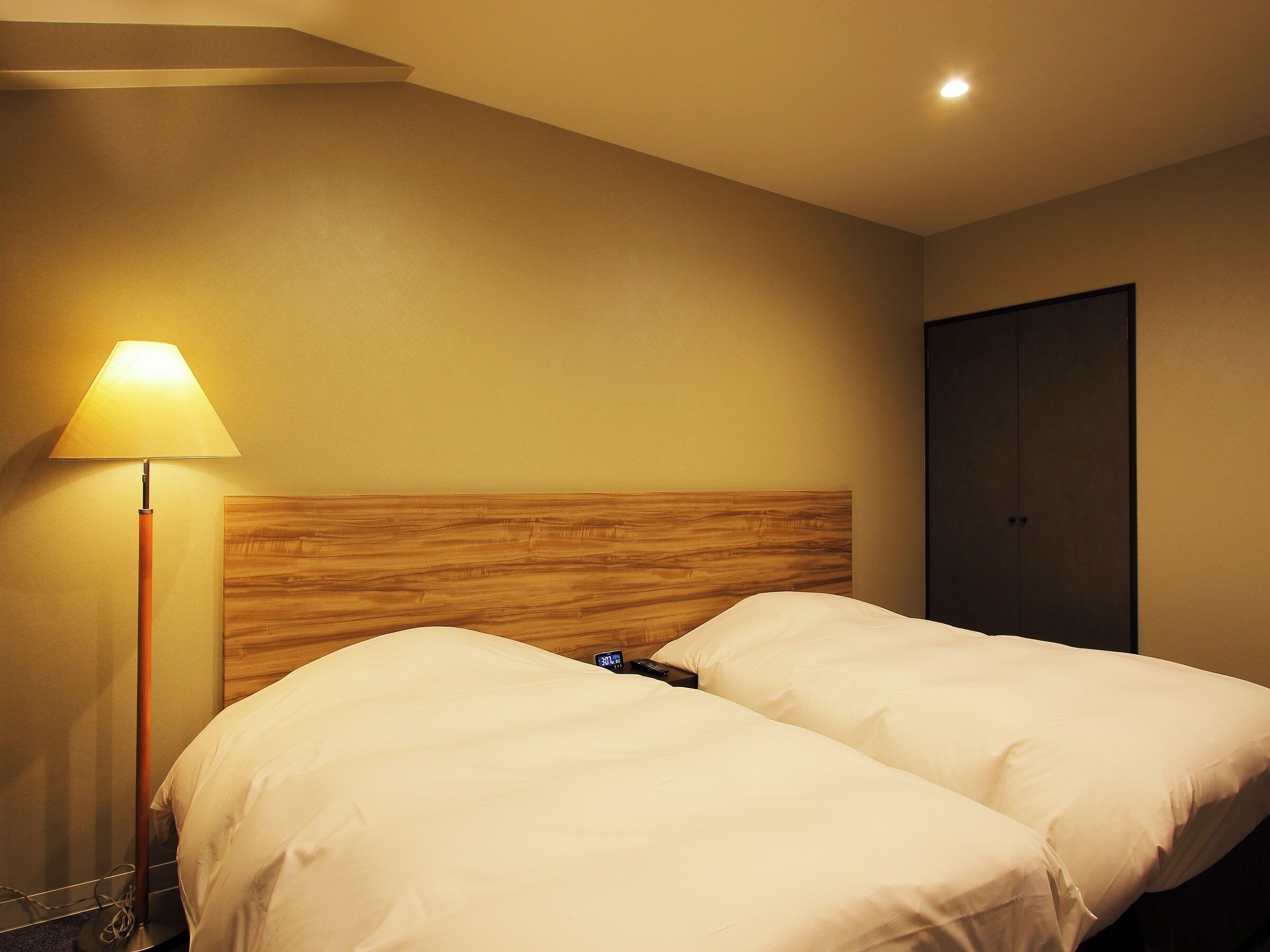 Une chambre d’hôtel avec deux lits, une tête de lit en bois, une table de chevet avec une lampe et une armoire.