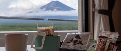 A window with a view of a mountain and clouds, a teal mug with a handle, a white cup, and a tray with coffee packets.