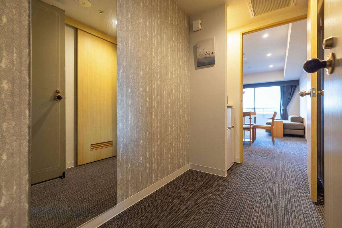 Un pasillo de hotel con pisos alfombrados, una puerta de madera y vista a una sala de estar con sofá y una mesa.