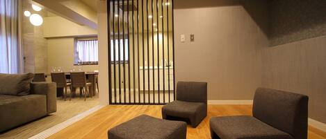 A modern interior with a seating area featuring dark grey sofas and ottomans, wooden flooring, and a partition with vertical slats.