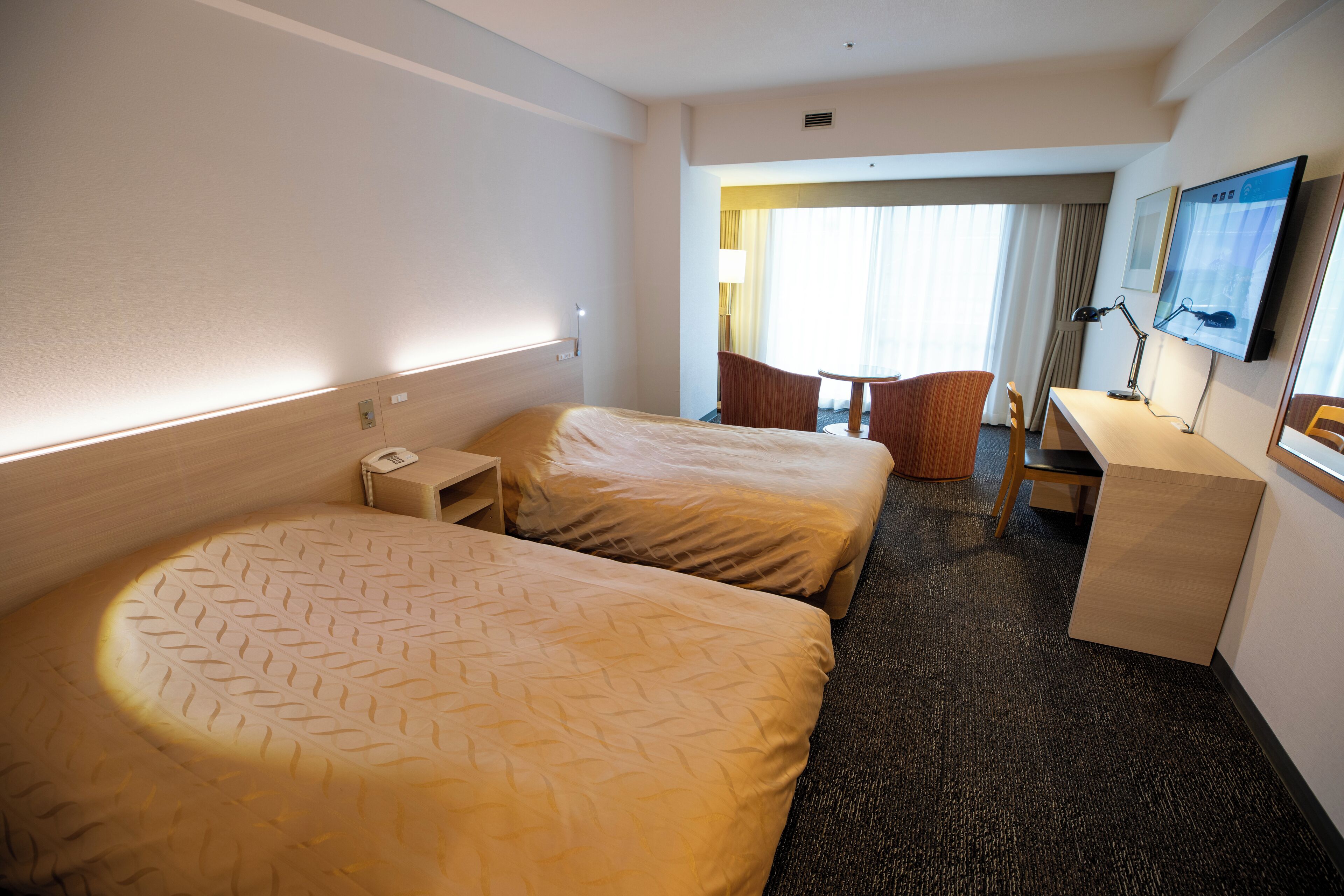 Habitación de hotel con dos camas, un escritorio, una silla, un televisor y una ventana con cortinas.
