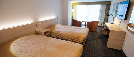 Habitación de hotel con dos camas, un escritorio, una silla, un televisor y una ventana con cortinas.