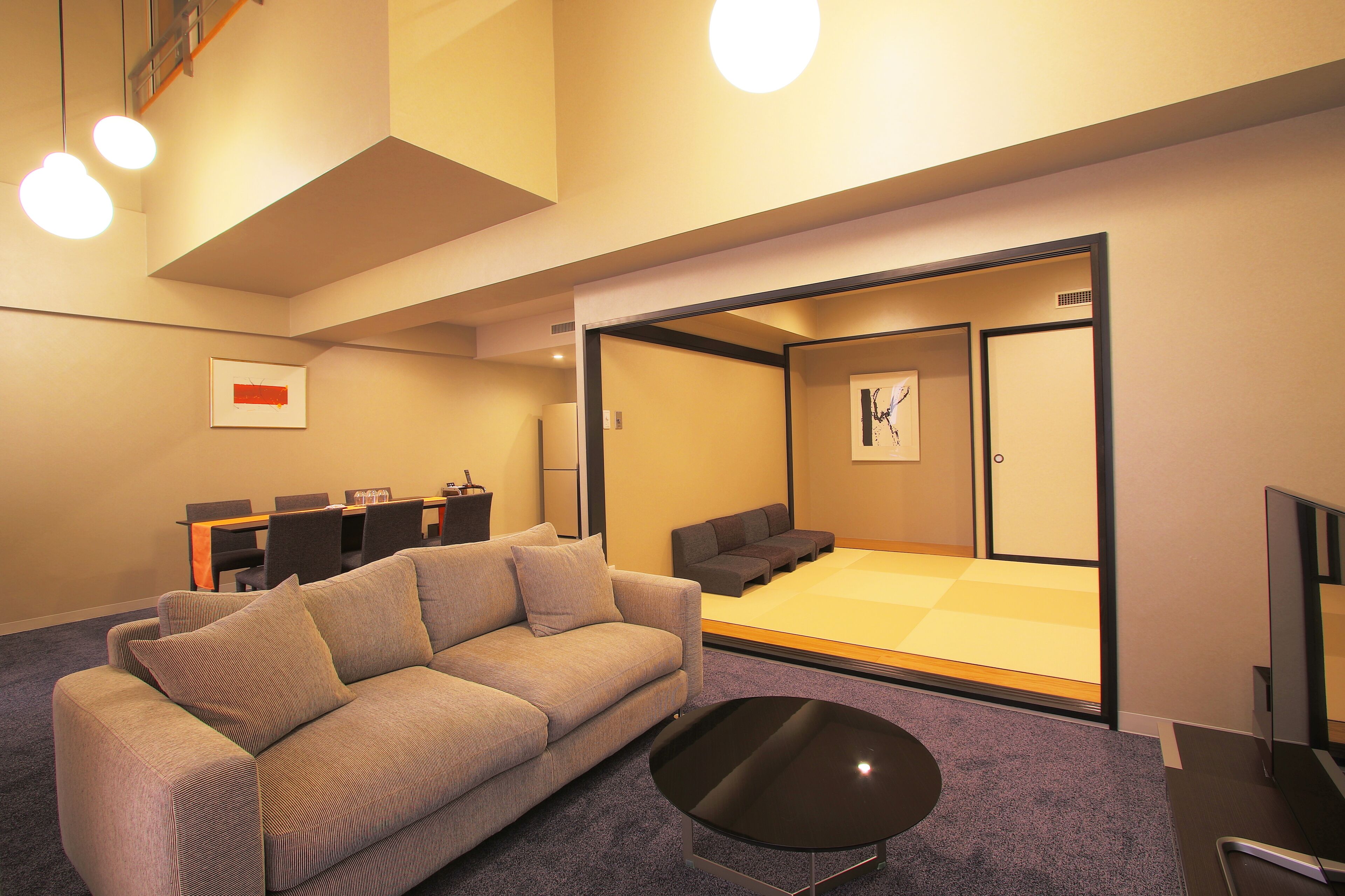 A modern living room with a sofa, a coffee table, and a seating area with a low table and chairs.
