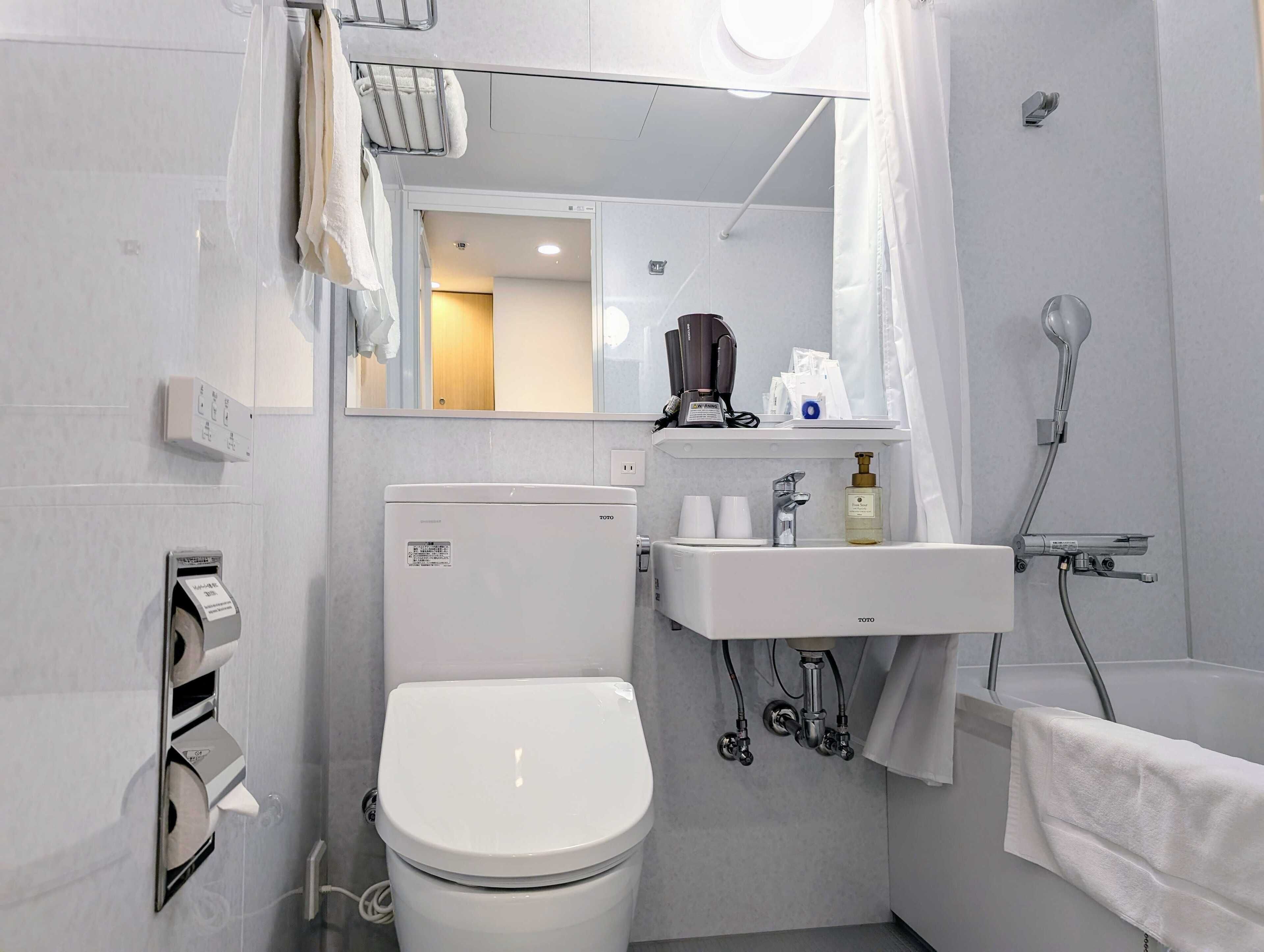 Une salle de bain moderne avec des toilettes blanches, un lavabo, un miroir et une douche.