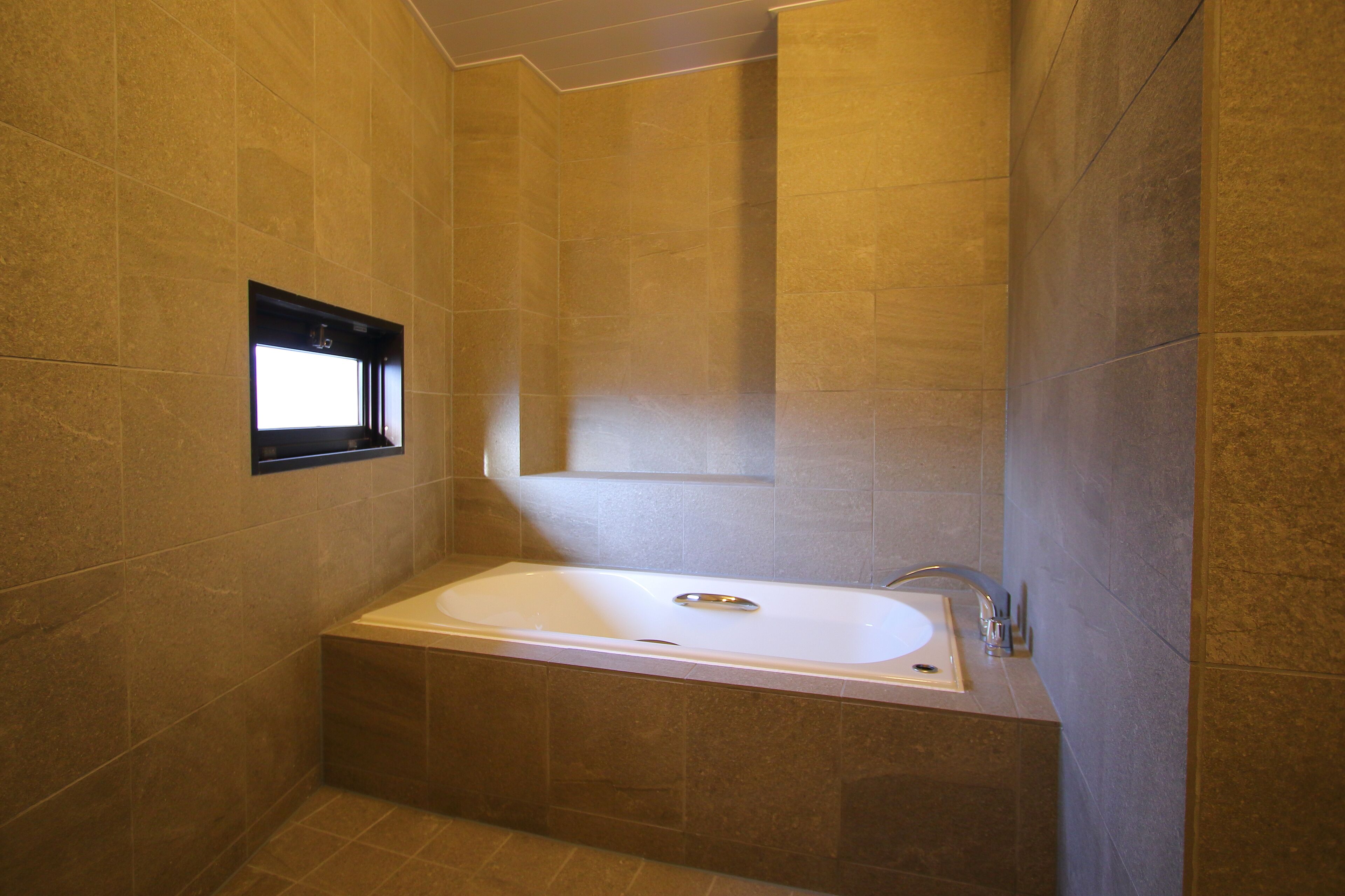 A modern bathroom with a freestanding bathtub, tiled walls, and a window.