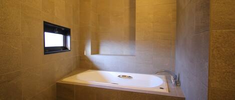 A modern bathroom with a freestanding bathtub, tiled walls, and a window.