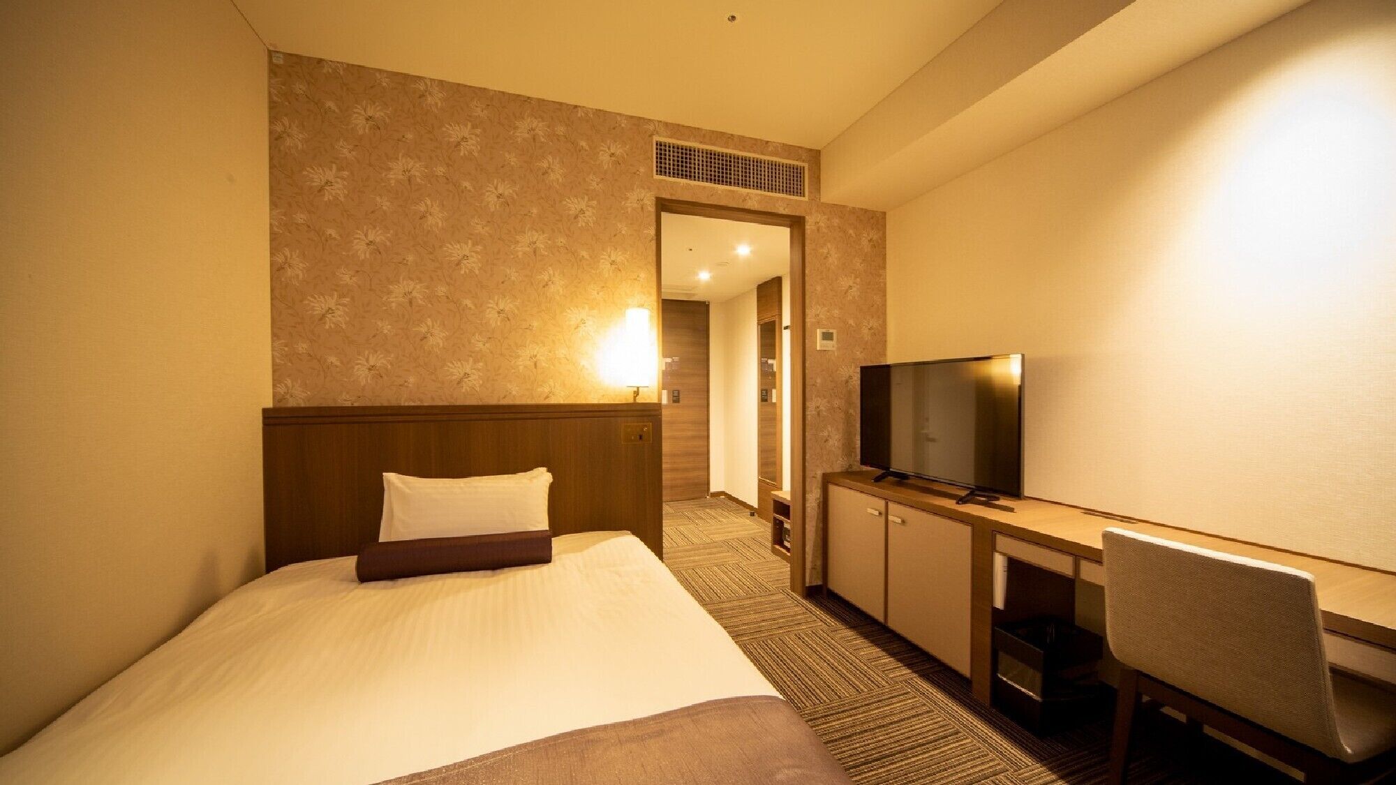 A hotel room with a bed, a TV, a desk, and a chair.