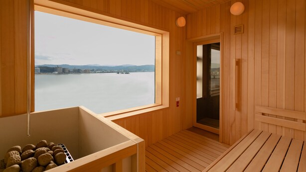 Una sauna de madera con un ventanal grande que da a un cuerpo de agua y al paisaje urbano.
