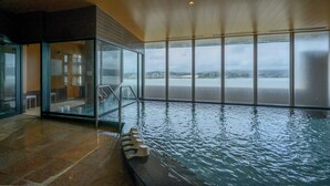 Una piscina interior con paredes de vidrio transparente, suelo de baldosas y vistas panorámicas de la ciudad a través de amplios ventanales.