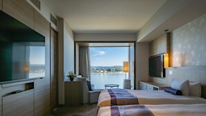 Habitación de hotel con una cama grande, televisión, escritorio con silla, una mesita y vistas a una masa de agua.