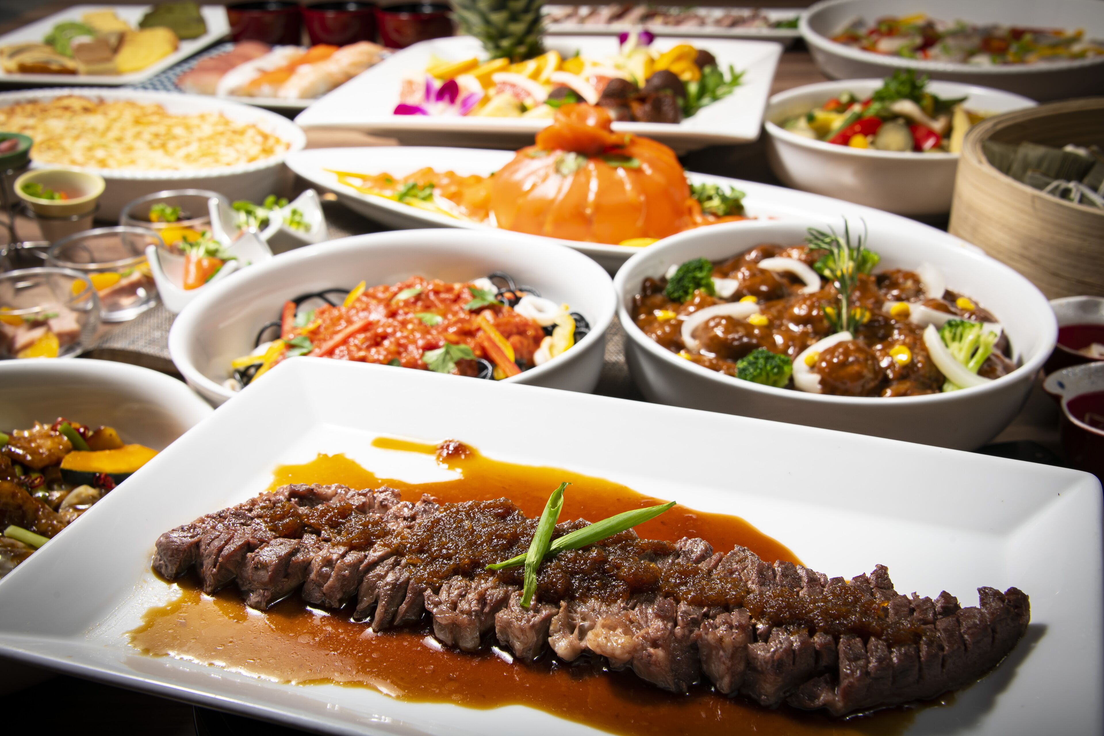 A variety of dishes on a table, including a prominent steak with sauce and garnish.