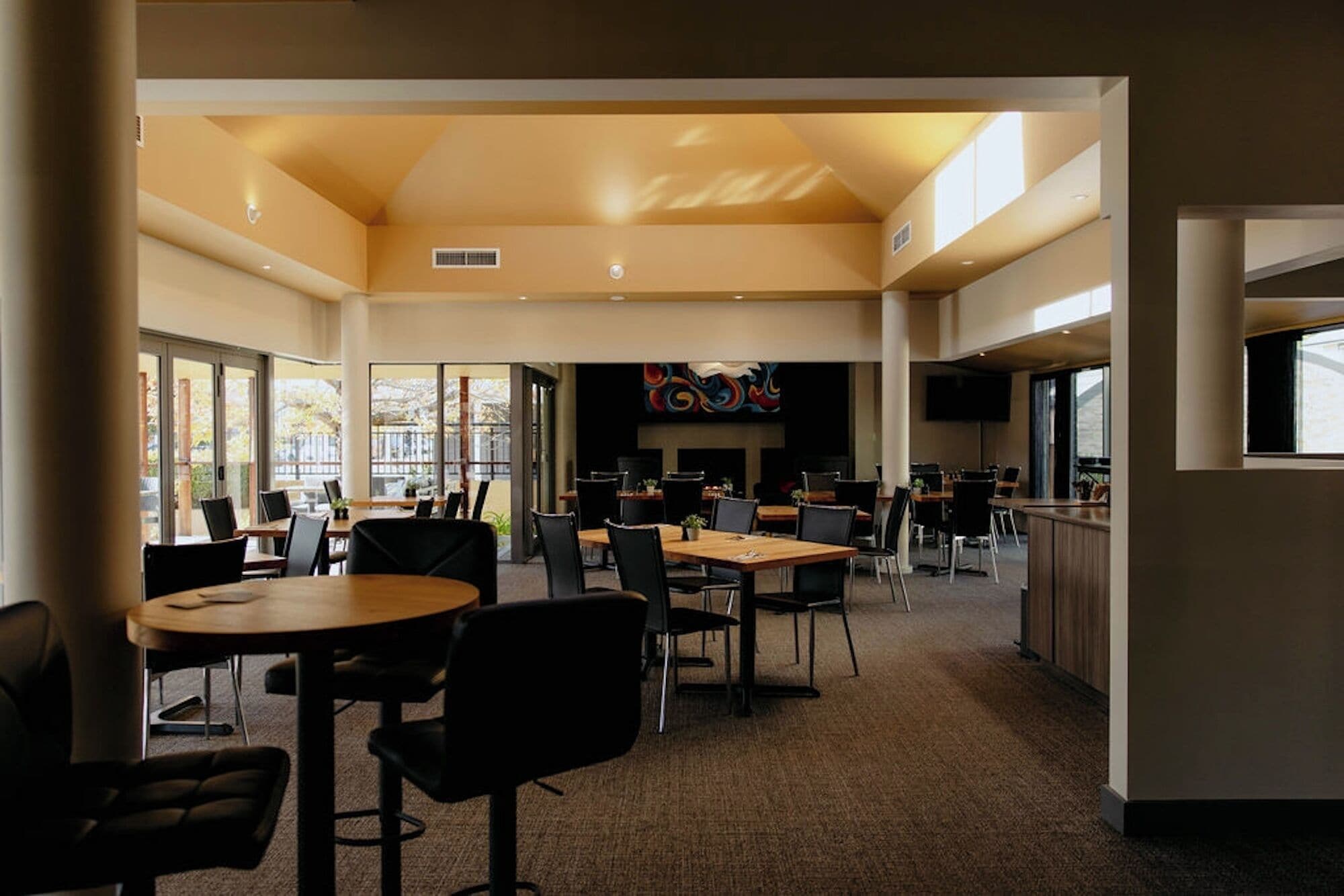 A spacious indoor area with multiple tables and chairs, large windows, and a flat-screen TV mounted on the wall.