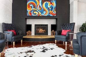 A modern living room with a fireplace, two armchairs, a round coffee table, and a large abstract painting above the fireplace.