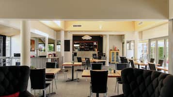 Un comedor de hotel con varias mesas y sillas, una zona de bar y vistas al exterior.